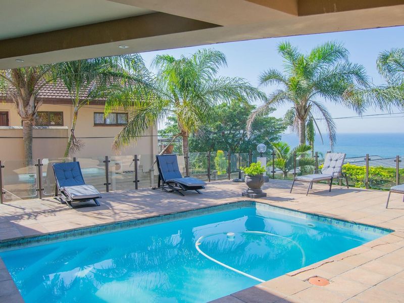 Outdoor pool area featuring a tiled deck, glass balustrade, and a covered patio with scenic ocean views.