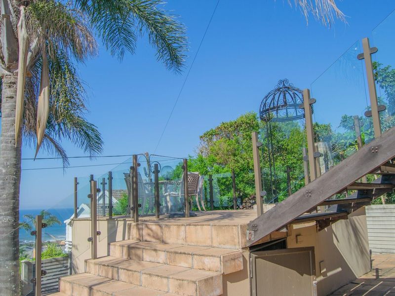Elevated outdoor patio featuring a tiled staircase, glass balustrade, and scenic coastal views, providing a functional space for outdoor relaxation.