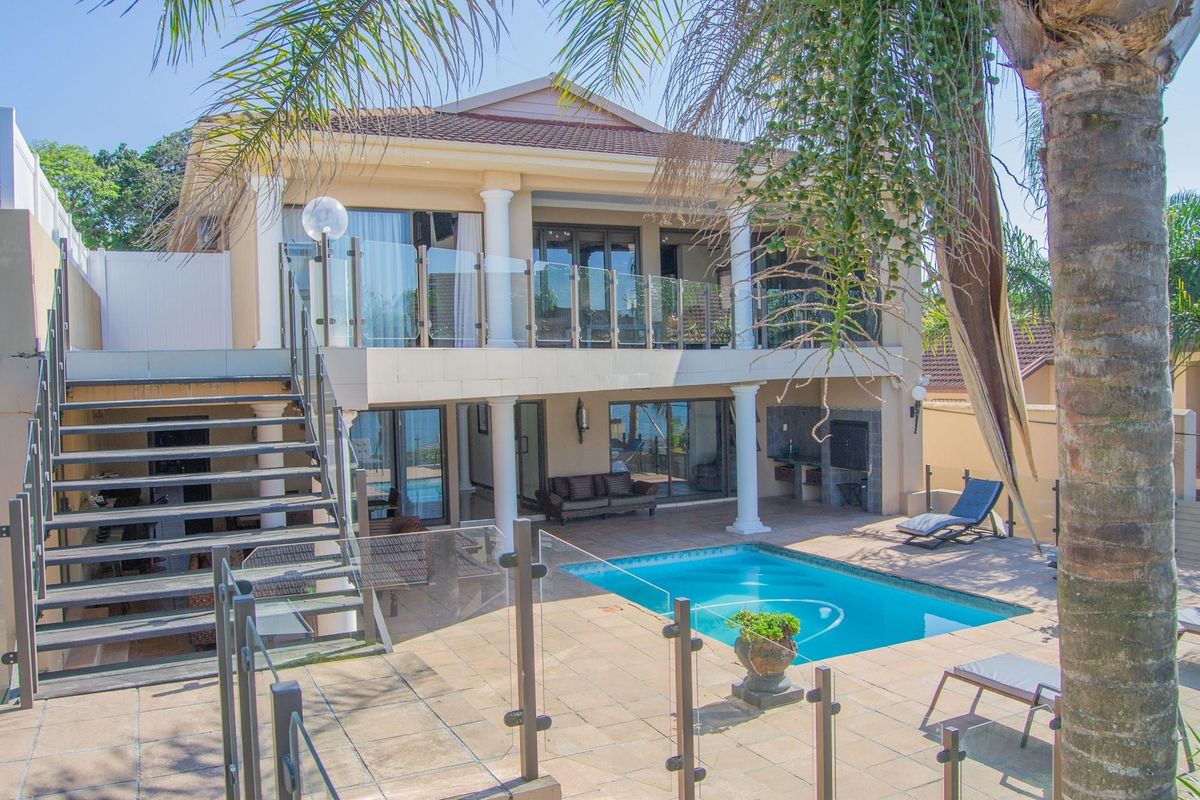 Rear exterior view featuring a swimming pool, tiled patio area, built-in braai, and a double-story facade with glass balustrades and an external staircase.