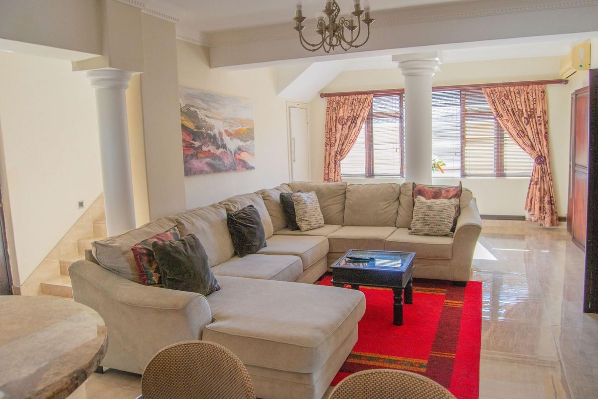 Spacious living room featuring decorative columns, crown molding, tiled flooring, and a wall-mounted air conditioning unit.