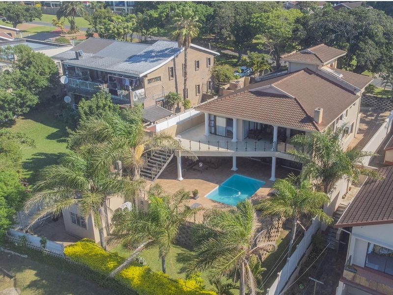 Aerial view of a multi-level residential property featuring a swimming pool, spacious elevated balcony, and landscaped garden area.