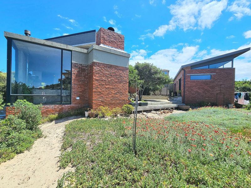 Rear view of a modern architectural house featuring exposed brickwork, large glass windows, a prominent chimney, and a landscaped garden with timber decking.