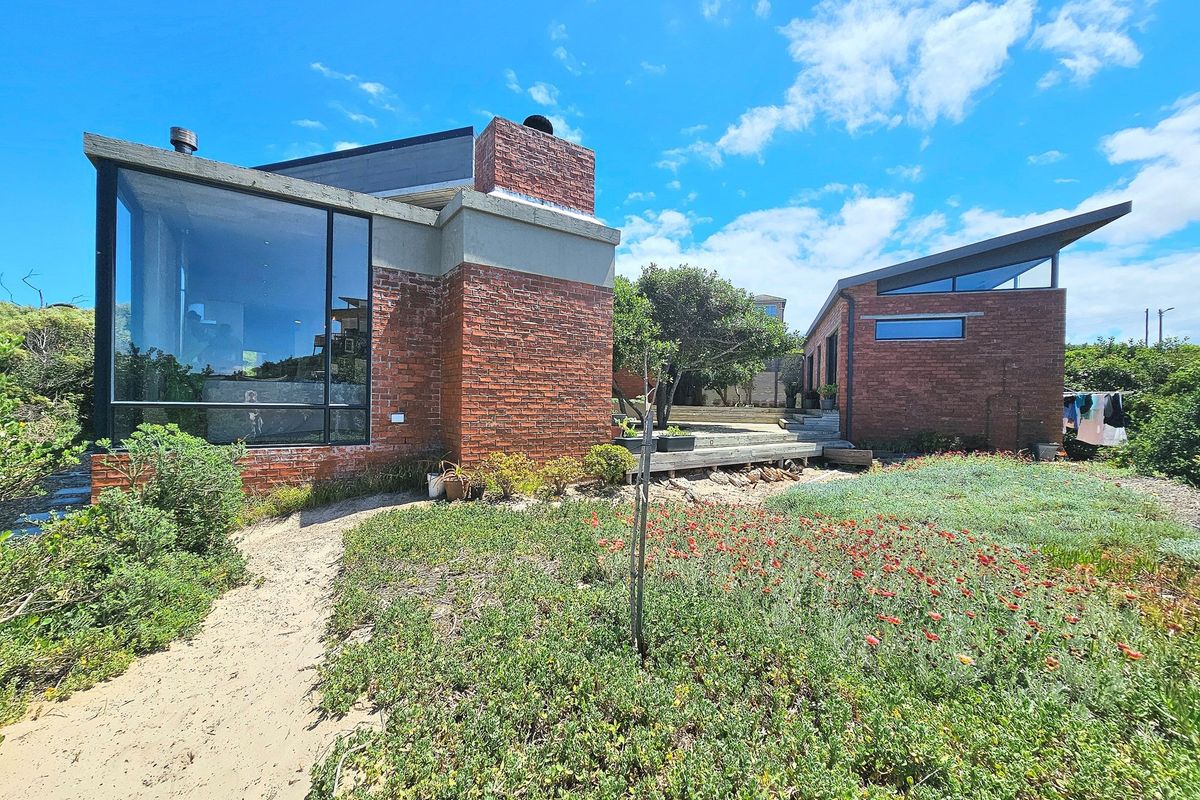 Rear view of a modern architectural house featuring exposed brickwork, large glass windows, a prominent chimney, and a landscaped garden with timber decking.