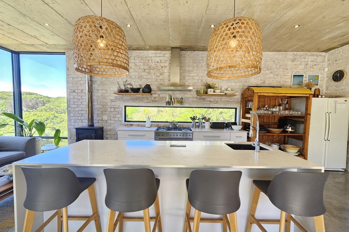Modern kitchen featuring an island with stone countertops, exposed brick walls, concrete ceilings, and a built-in wood-burning fireplace with scenic views.