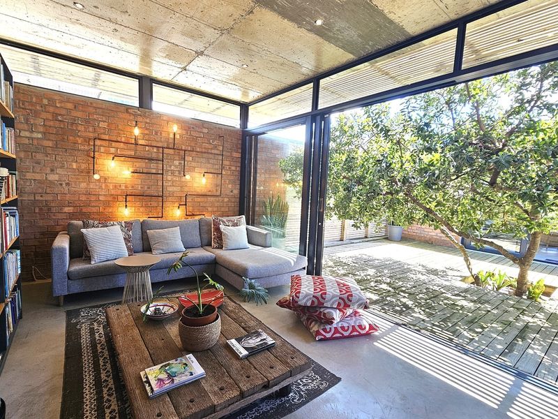Modern living room featuring exposed concrete ceilings, brick feature wall, and expansive glass sliding doors opening onto a wooden deck.