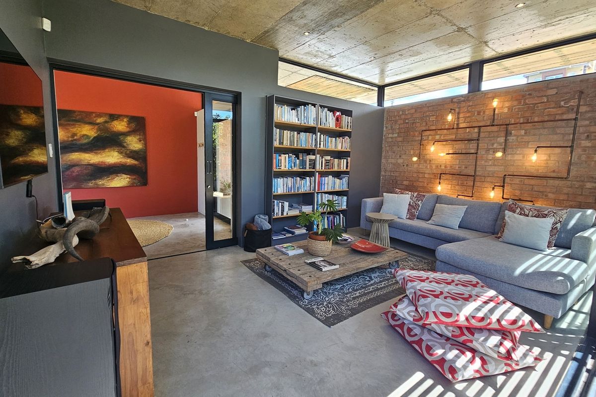 Modern living room featuring an exposed concrete ceiling, polished concrete floors, and a striking exposed brick wall with integrated industrial-style lighting.