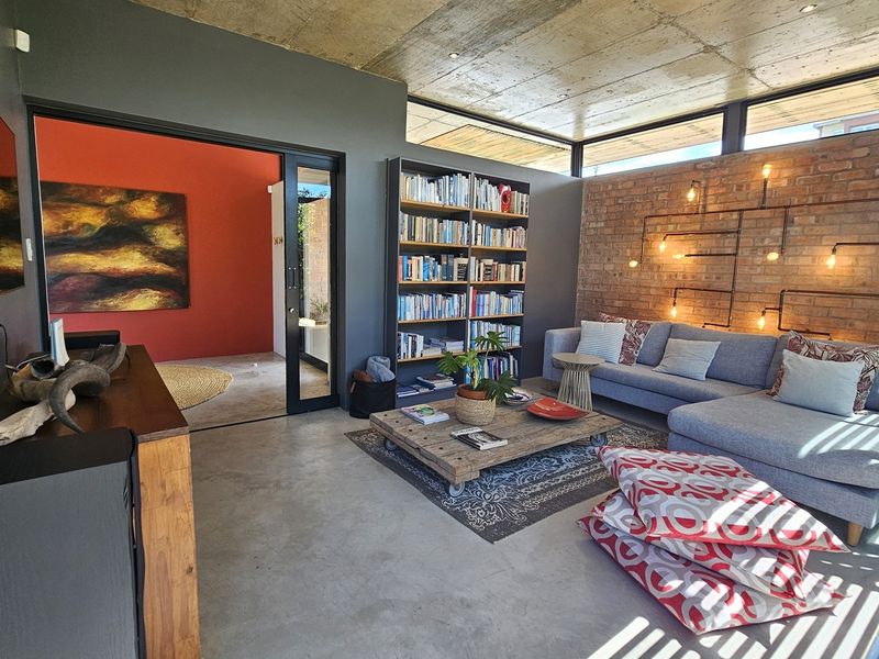 Modern living room featuring an exposed concrete ceiling, polished concrete floors, and a striking exposed brick wall with integrated industrial-style lighting.