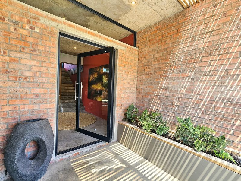 Modern entrance featuring an industrial aesthetic with exposed brick walls, a concrete ceiling, and a sleek pivot door leading into the home.