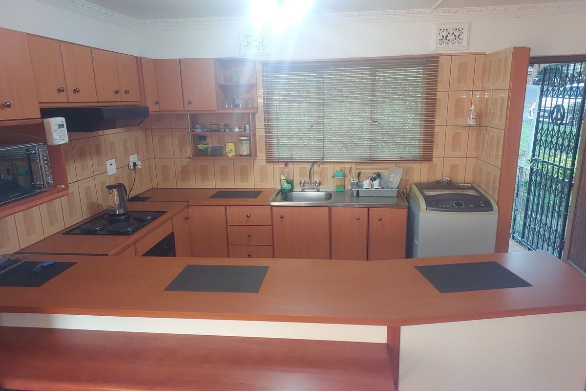 A functional kitchen featuring wood-finish cabinetry, a breakfast bar, built-in hob, and integrated sink, with direct access to an exterior security gate.