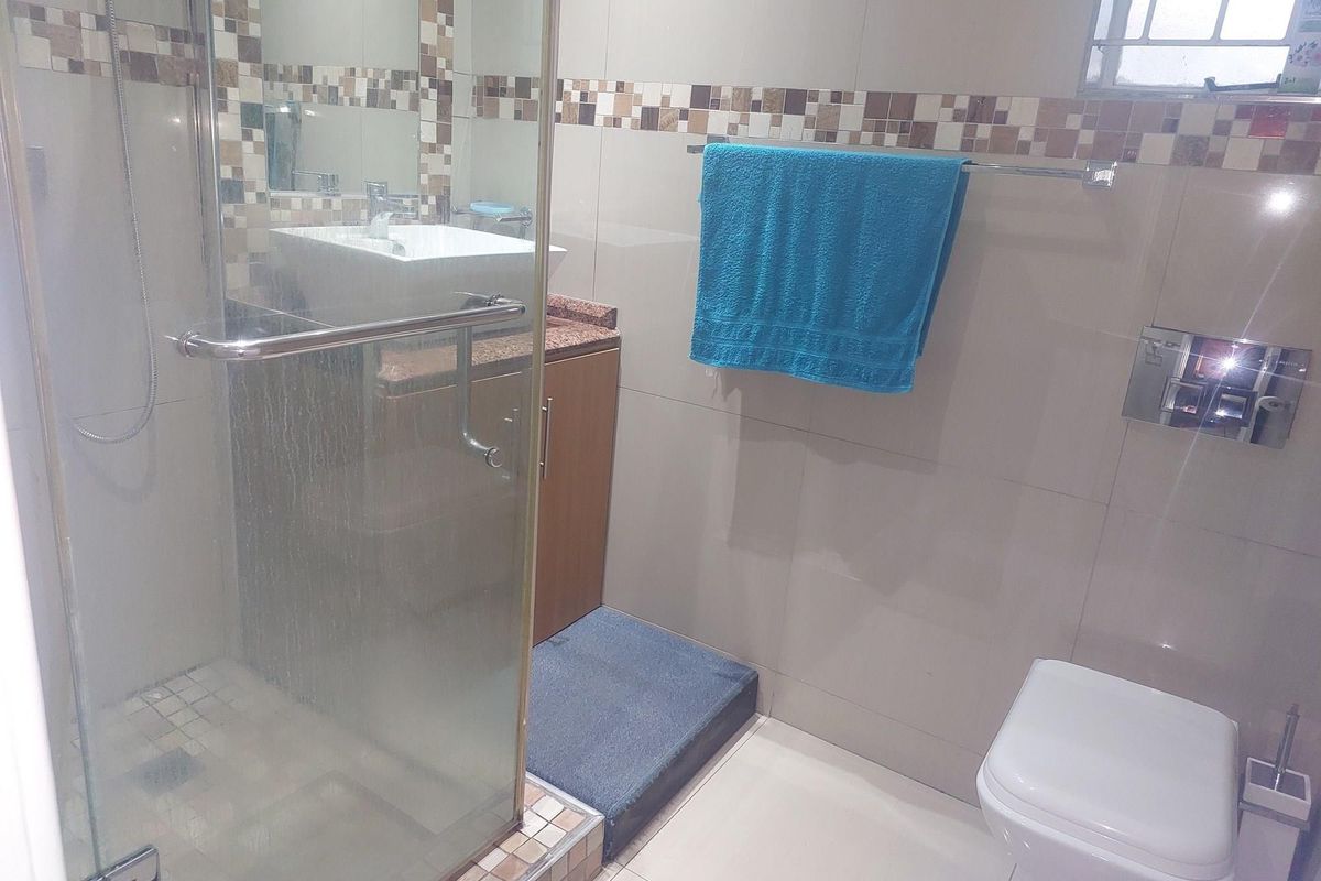 A compact bathroom featuring a glass-enclosed shower, a wall-mounted toilet, and a vanity with a vessel sink and stone countertop.