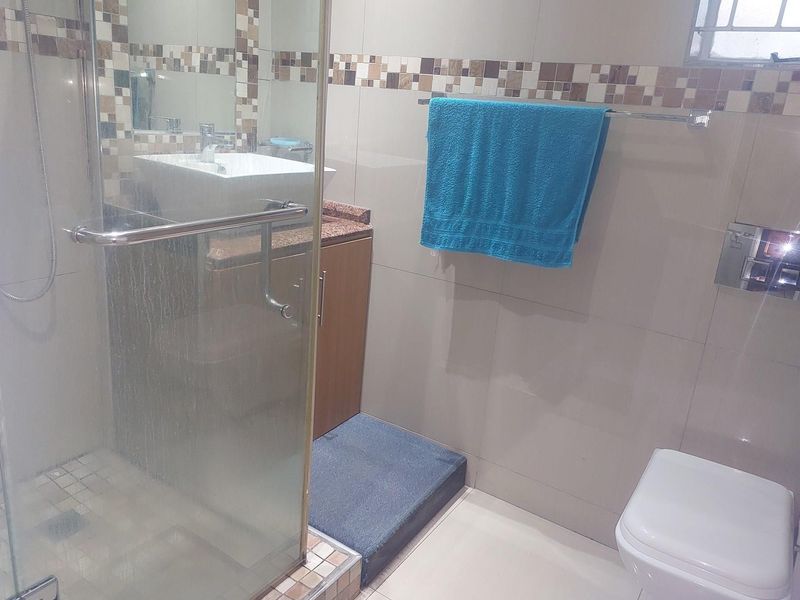A compact bathroom featuring a glass-enclosed shower, a wall-mounted toilet, and a vanity with a vessel sink and stone countertop.