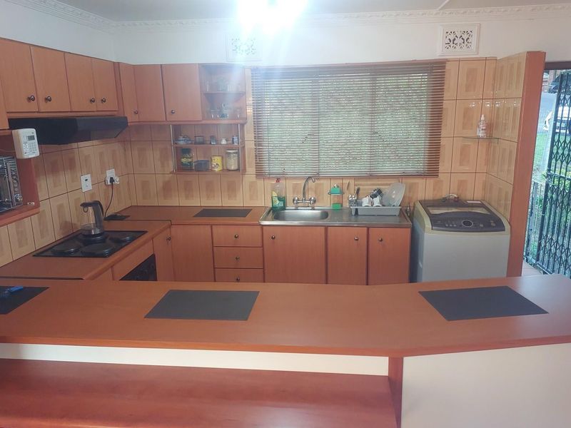 A functional kitchen featuring wood-finish cabinetry, a breakfast bar, built-in hob, and integrated sink, with direct access to an exterior security gate.