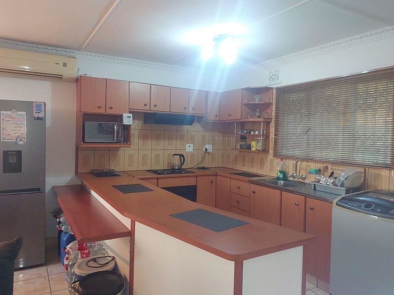 A functional kitchen featuring wooden cabinetry, a breakfast bar, tiled backsplash, and built-in appliances including a hob and extractor fan.