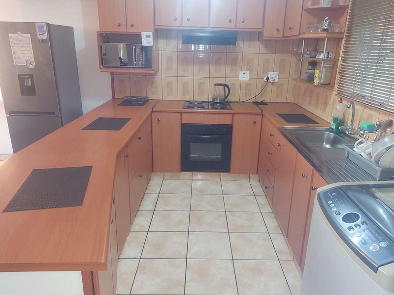 A functional U-shaped kitchen featuring wood-finish cabinetry, built-in oven, hob, extractor fan, and tiled flooring with a breakfast counter.