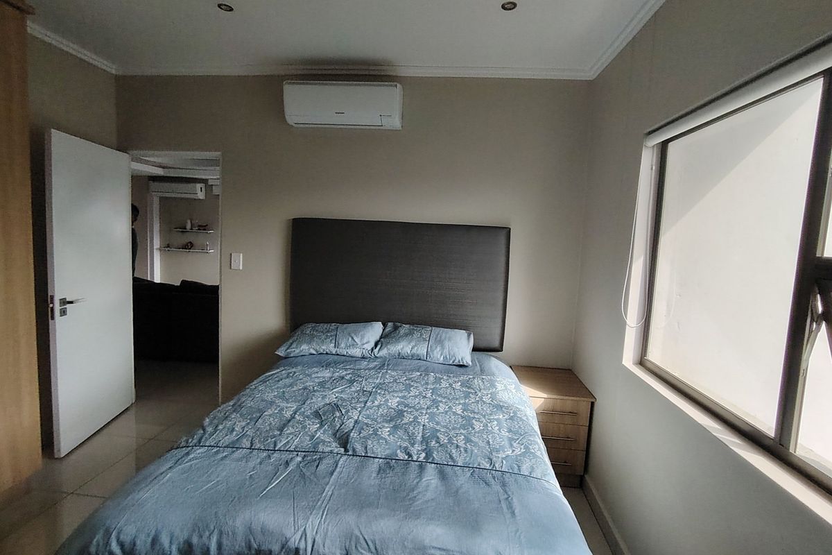 A bedroom featuring tiled flooring, a wall-mounted air conditioning unit, and a window with a roller blind.