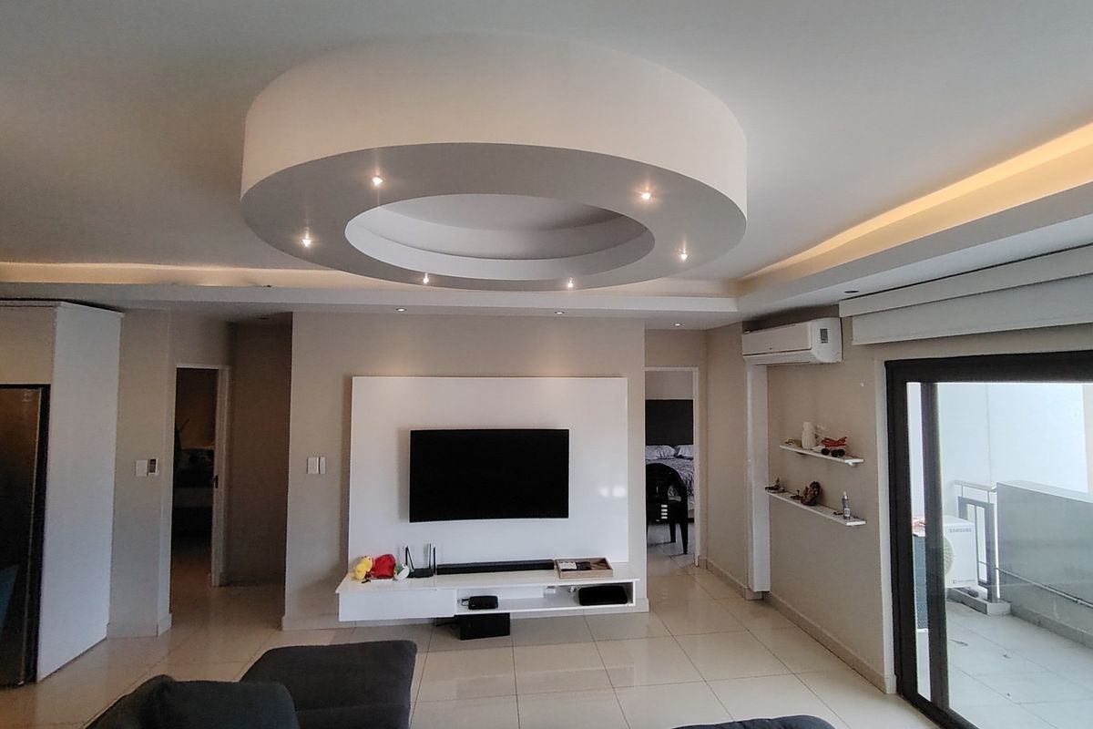 Modern living room featuring a distinctive circular recessed ceiling design with integrated downlights, tiled flooring, and a built-in media wall unit.