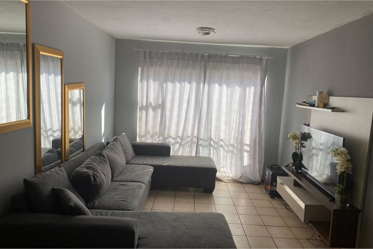 A living room featuring tiled flooring and a large sliding glass door with curtains, providing natural light to the space.