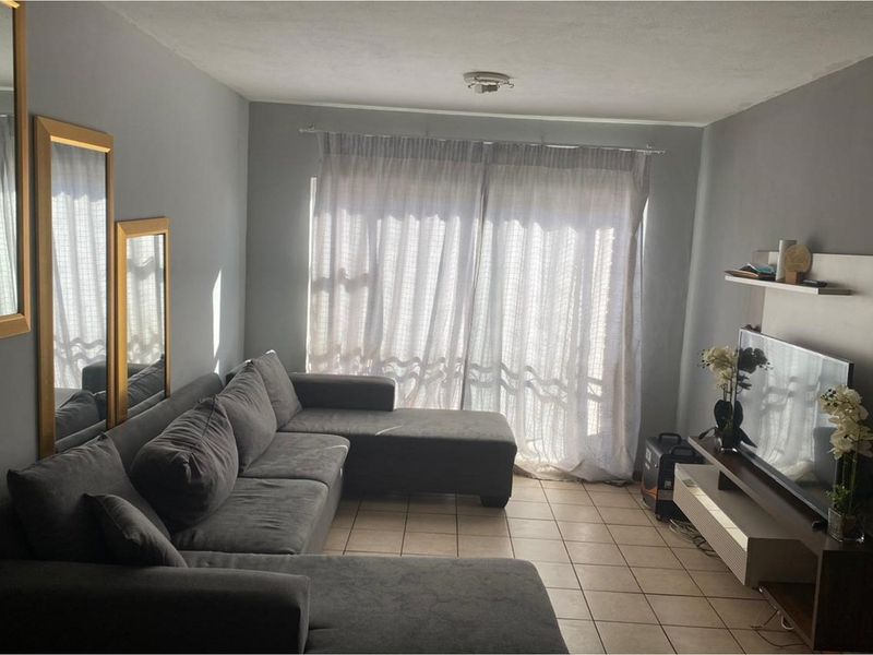 A living room featuring tiled flooring and a large sliding glass door with curtains, providing natural light to the space.