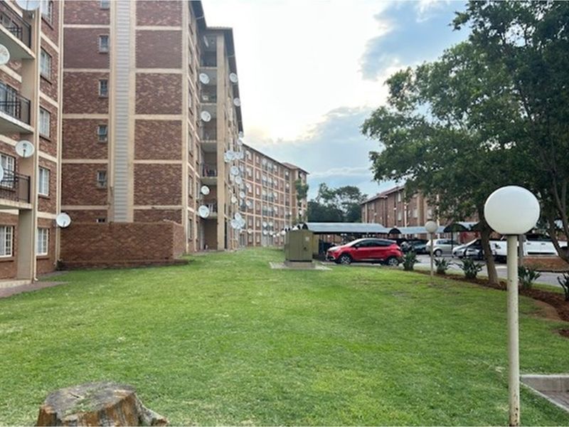 Exterior view of a multi-story brick apartment complex featuring communal lawn areas, paved parking, and carports.