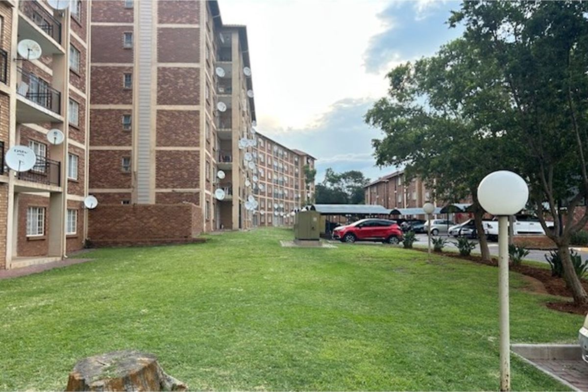 Exterior view of a multi-story brick apartment complex featuring communal lawn areas, paved parking, and carports.