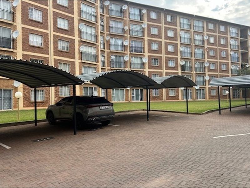 Exterior view of the apartment complex featuring covered parking bays, paved driveway, and communal lawn area.