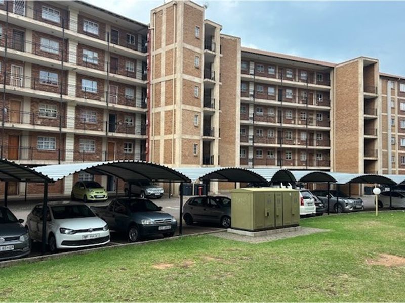 Exterior view of a multi-story brick apartment complex featuring covered parking bays and balcony access.