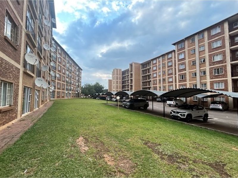 Exterior view of an apartment complex featuring brick facades, communal lawn areas, and covered parking bays for residents.