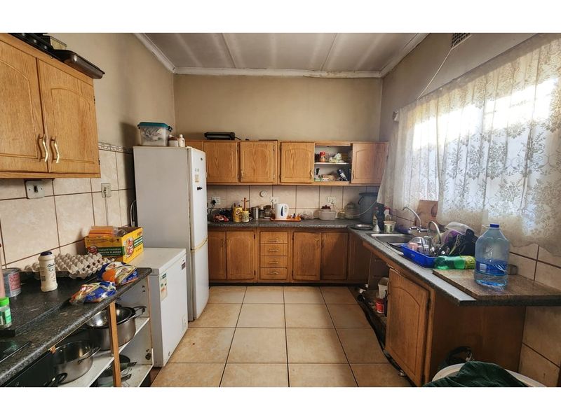 A dated kitchen featuring wood-look laminate cabinetry, tiled flooring, and a double basin sink, offering significant potential for modernization and renovation.