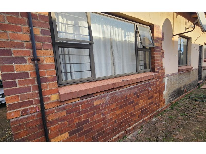 Rear exterior view of the property featuring brick facade, aluminium window frames with security bars, and paved ground area.