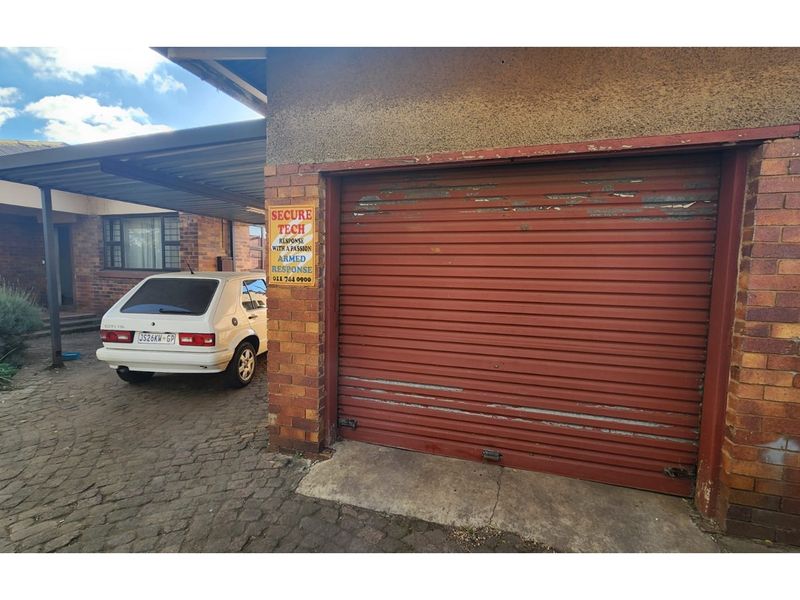 Exterior view of a single garage with a roller shutter door, adjacent carport, and paved driveway area.
