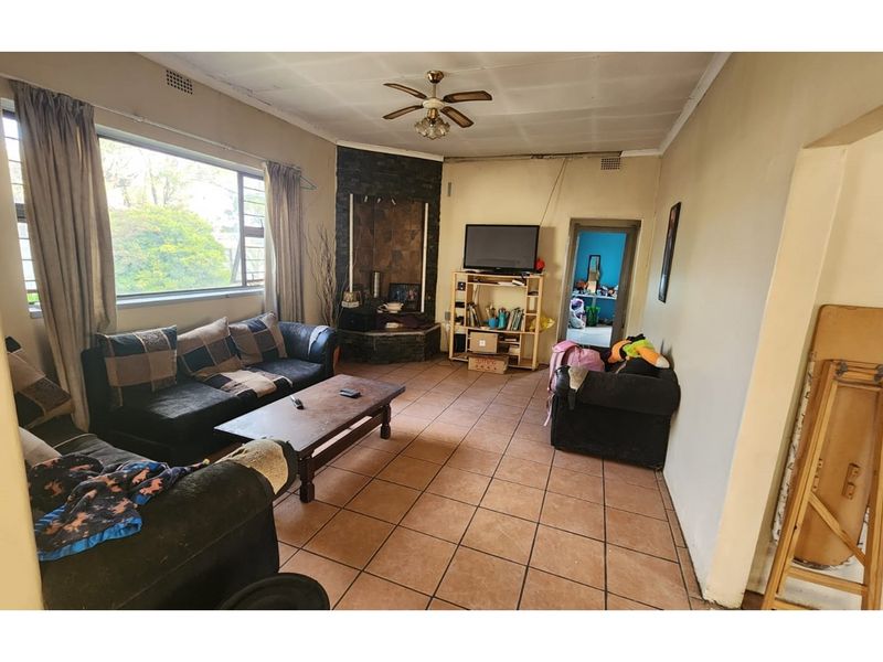 Spacious living room featuring tiled flooring, a stone-clad fireplace, and a ceiling fan, offering a functional layout with natural light.