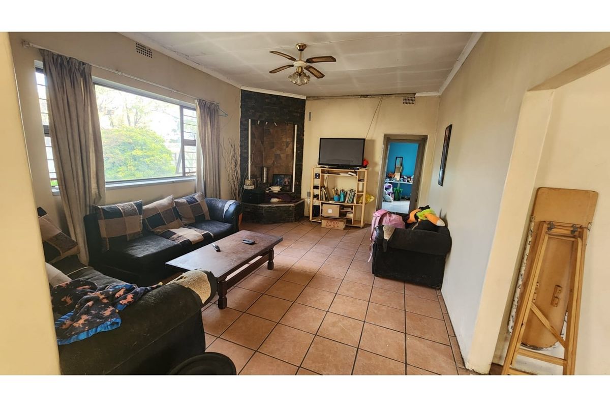 Spacious living room featuring tiled flooring, a stone-clad fireplace, and a ceiling fan, offering a functional layout with natural light.