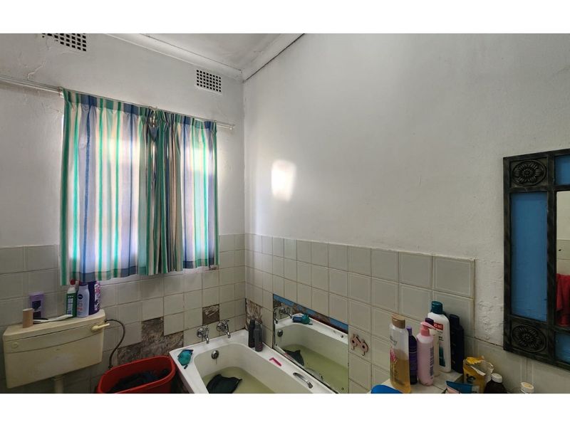 A dated bathroom featuring a standard bathtub, wall-mounted cistern, and tiled walls requiring maintenance and cosmetic updates.