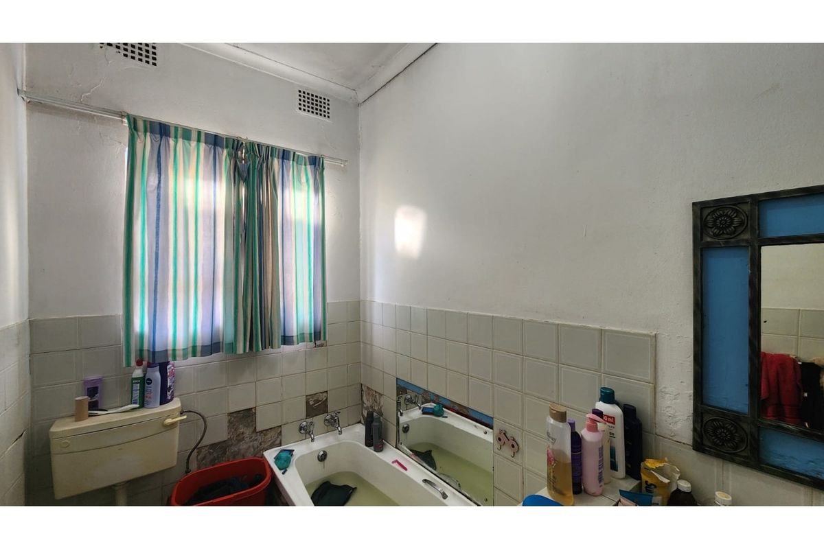 A dated bathroom featuring a standard bathtub, wall-mounted cistern, and tiled walls requiring maintenance and cosmetic updates.