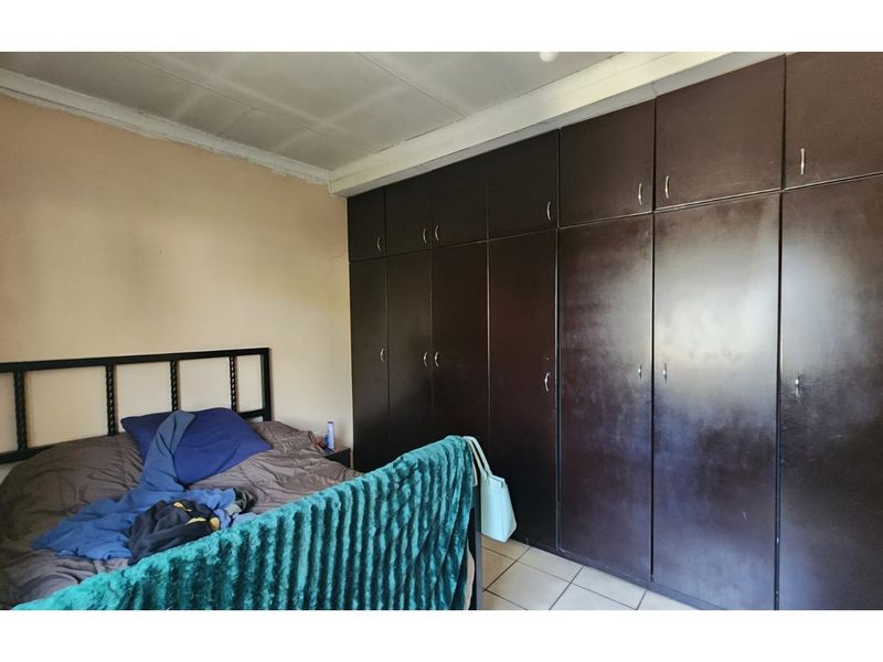 A bedroom featuring extensive dark wood built-in cupboards and tiled flooring, requiring cosmetic updates to the ceiling and cabinetry.