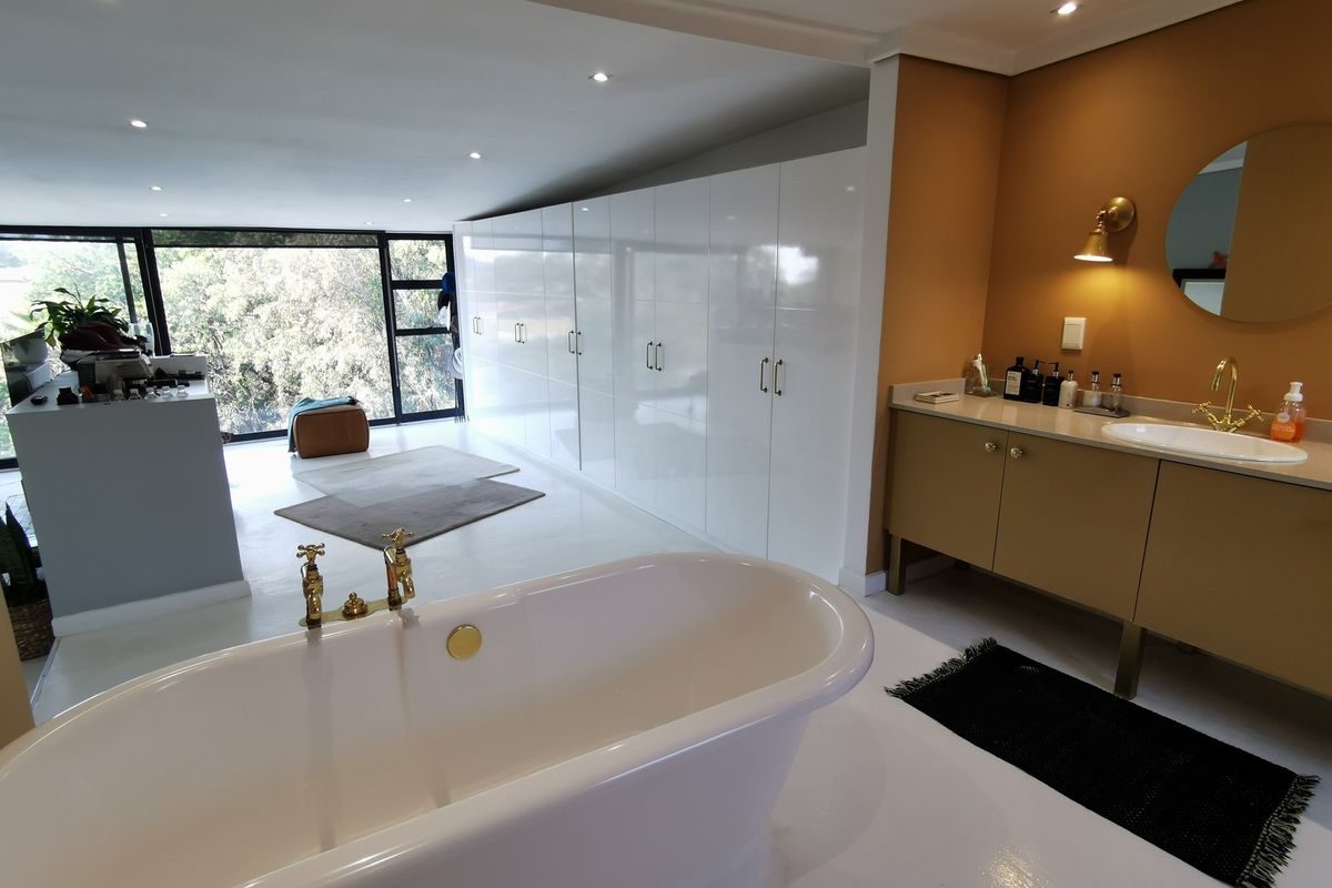 Spacious open-plan bathroom featuring a freestanding bathtub, modern vanity with brass fixtures, and extensive built-in cabinetry with a sleek white finish.