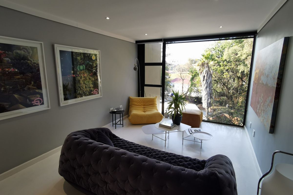 A modern living room featuring large floor-to-ceiling windows that provide ample natural light and scenic views of the surrounding greenery.