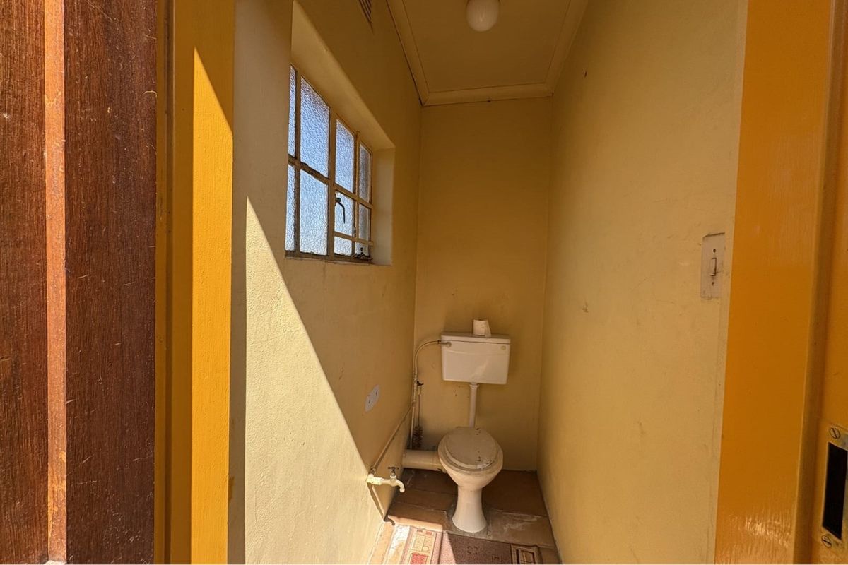 A compact, dated guest toilet featuring basic sanitary ware, tiled flooring, and a small window for natural light.