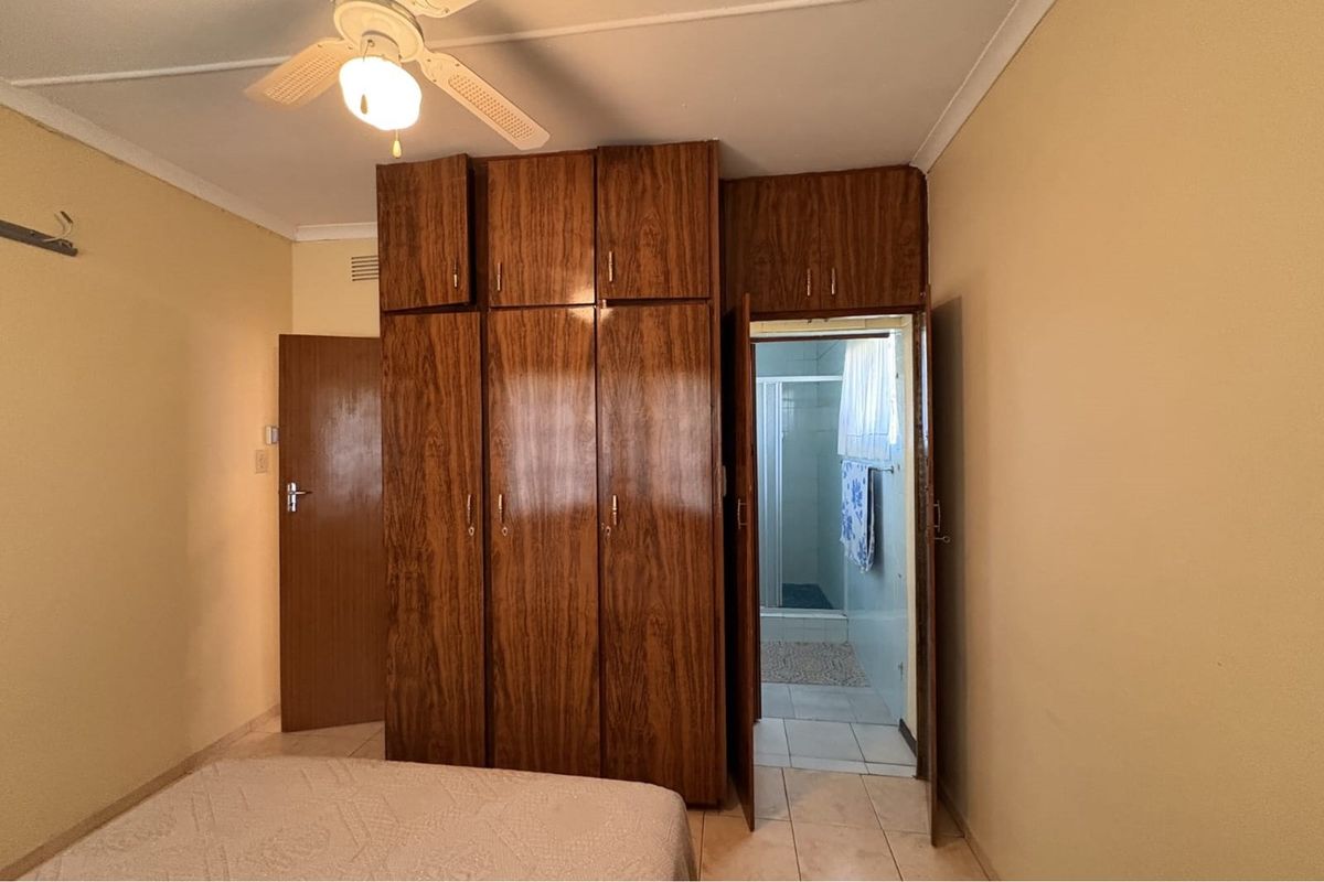 Bedroom featuring built-in wooden cabinetry and an en-suite bathroom access, complete with a ceiling fan and tiled flooring.