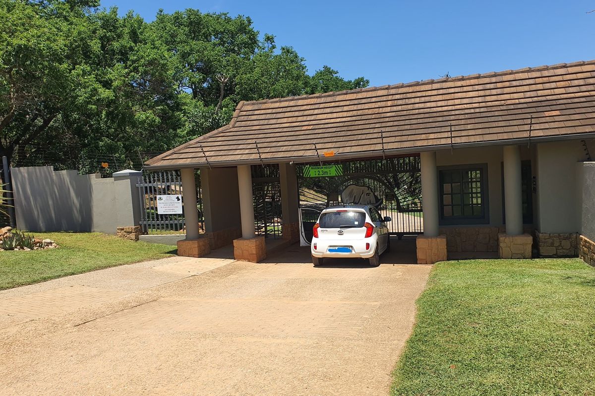 A secure gated entrance to the residential estate featuring a tiled roof structure, stone-clad pillars, and an automated security gate.