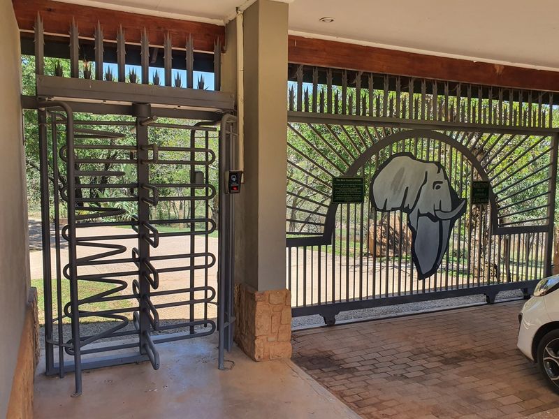 Secure gated entrance featuring a metal turnstile and a decorative sliding gate with an elephant motif, providing controlled access to the estate.