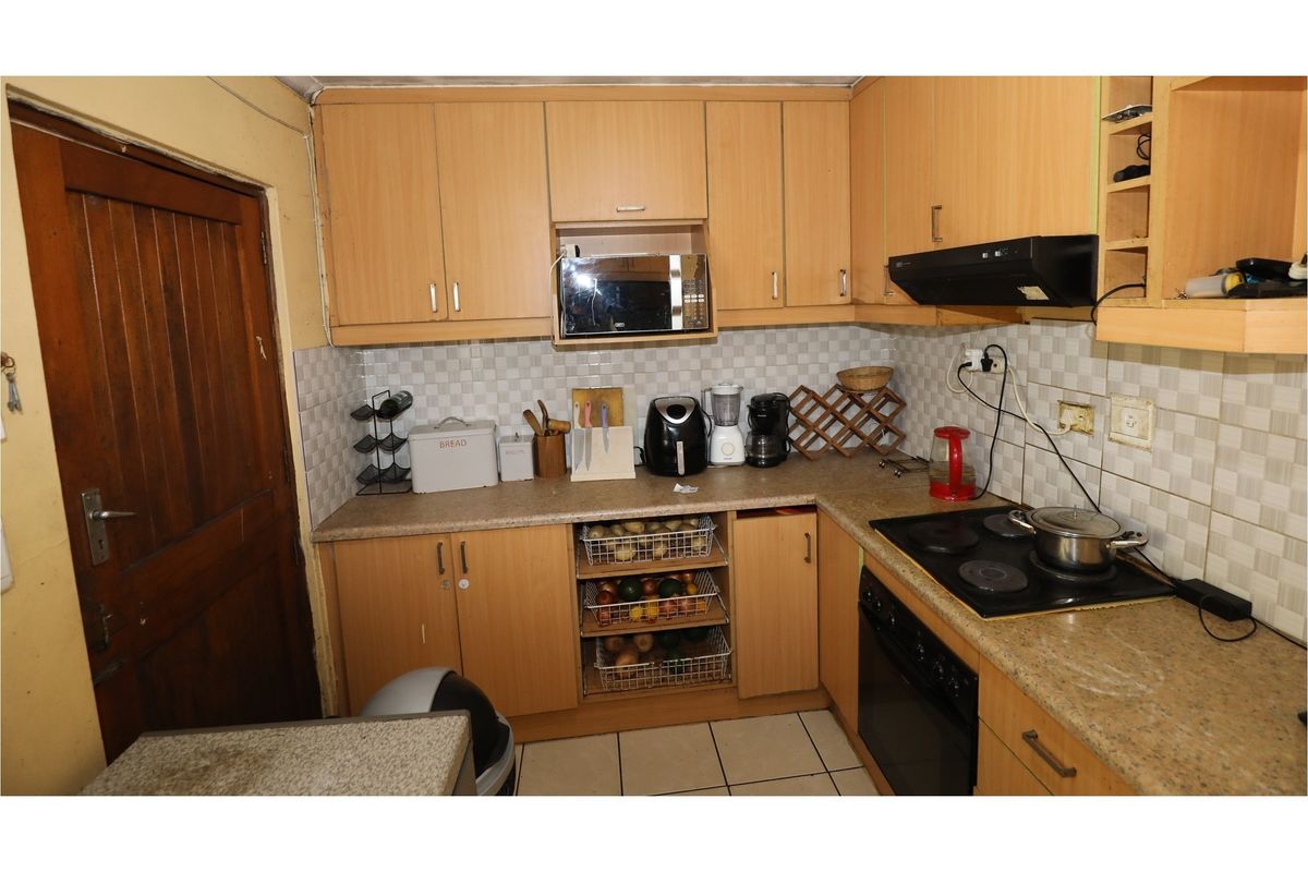 A compact kitchen featuring light wood-finish cabinetry, a built-in oven with electric hob, extractor fan, and tiled backsplash.