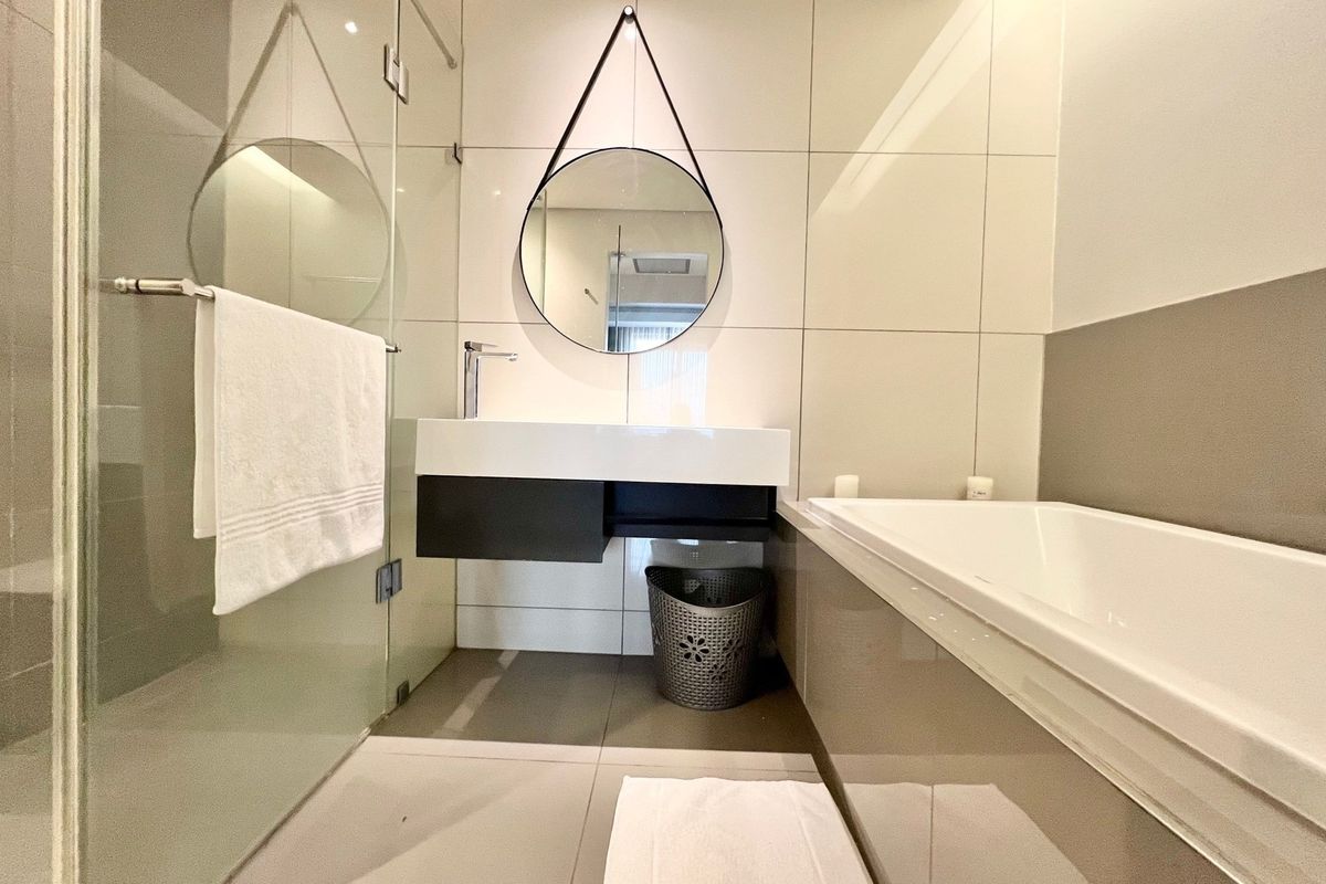 Modern bathroom featuring a wall-mounted vanity, glass-enclosed shower, and a built-in bathtub with neutral wall tiling.