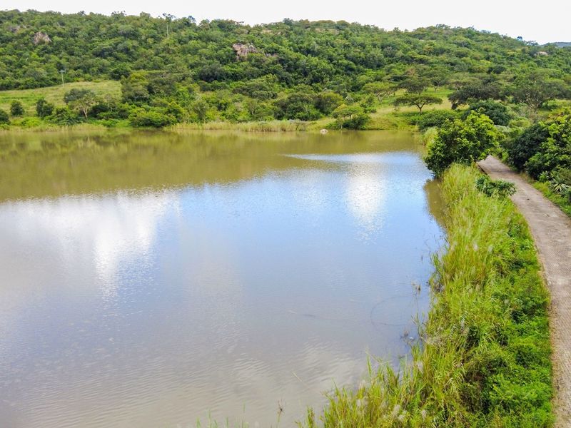An aerial view of a tranquil lake bordered by a paved pathway and lush, natural vegetation, showcasing the scenic landscape of the property.
