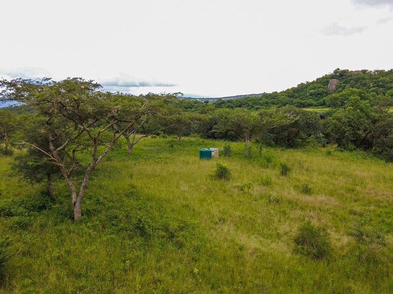 An aerial view of a vacant residential plot featuring natural vegetation, mature trees, and a water storage tank.