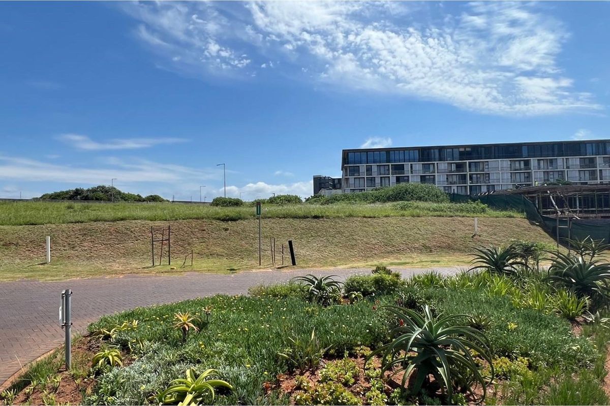 A view of a vacant residential plot featuring a paved driveway, landscaped verge, and a grassed embankment with surrounding estate development.
