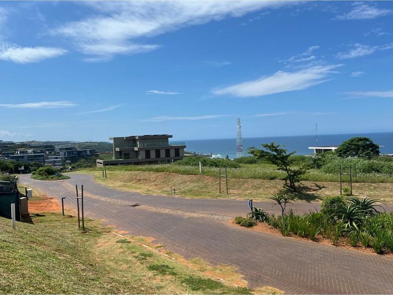 A scenic view of a residential estate featuring paved roads, landscaped greenery, and a distant ocean horizon.