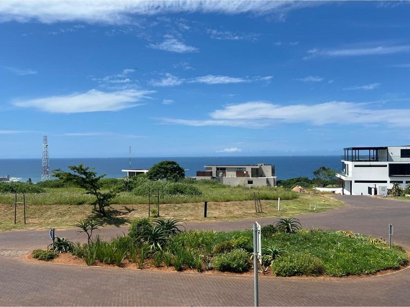 A scenic view of the ocean from a residential street, featuring paved roads and established landscaping in a coastal estate setting.