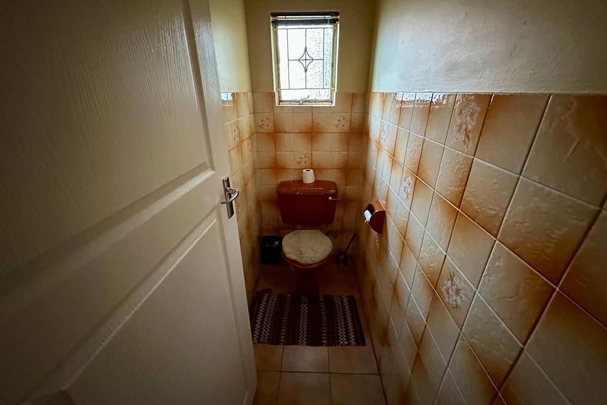 A compact guest toilet featuring dated ceramic wall tiles and a small leaded glass window.