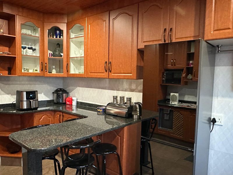 A functional kitchen featuring extensive wooden cabinetry, granite countertops, a breakfast bar, and a dedicated scullery area with additional storage.